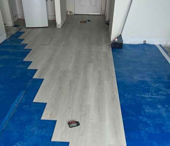 Installing light gray wood-look flooring in a room with blue underlayment.