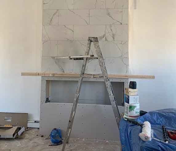 Fireplace under construction; tiled wall, ladder, and supplies.