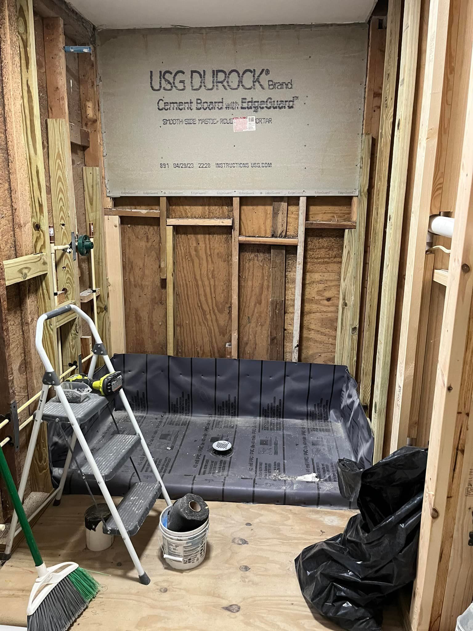 Bathroom remodel: shower base, walls framed with studs, USG Durock installed, tools present.