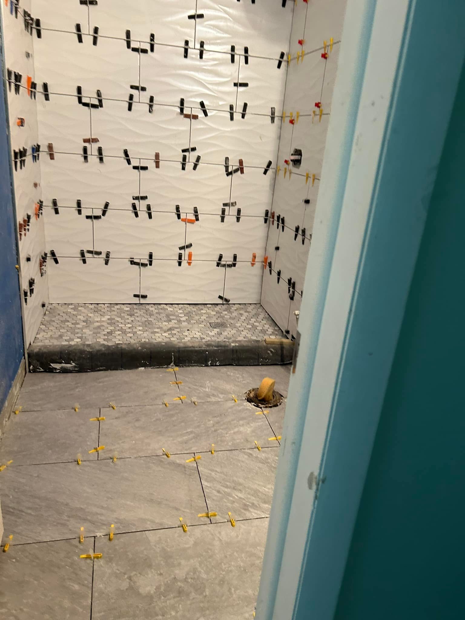 Shower stall with tiles in progress, leveling spacers, and floor tiles.