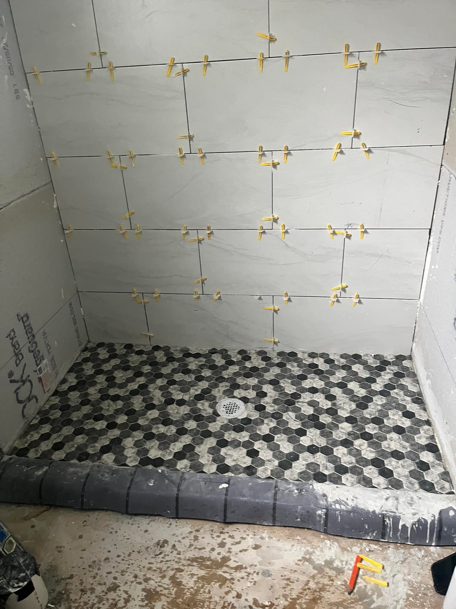 Shower stall under construction with tiled floor and wall, spacers visible.