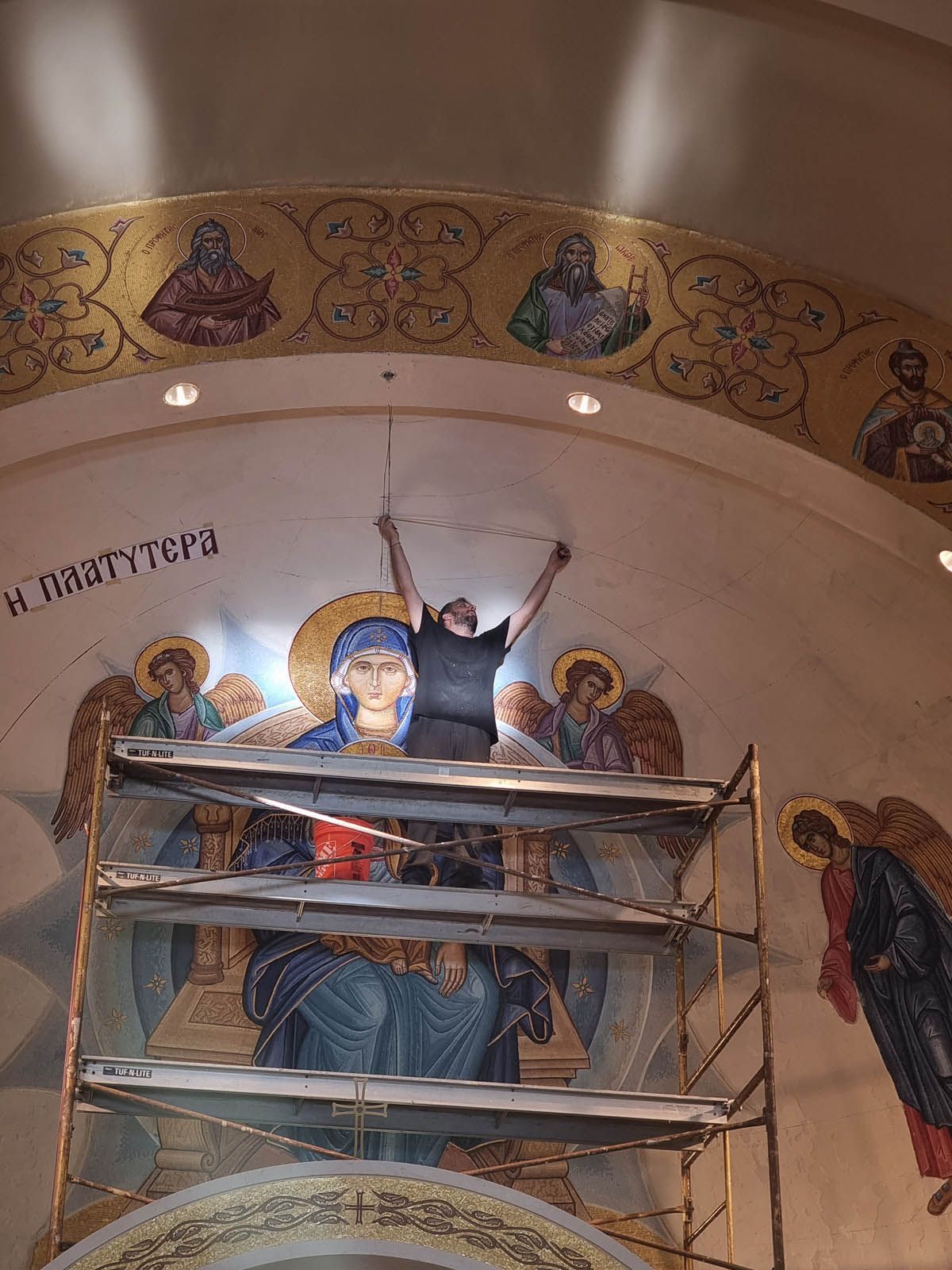 Byzantine Artworks artisan on scaffolding measuring apse wall preparing for gold mosaic tile installation around Platytera