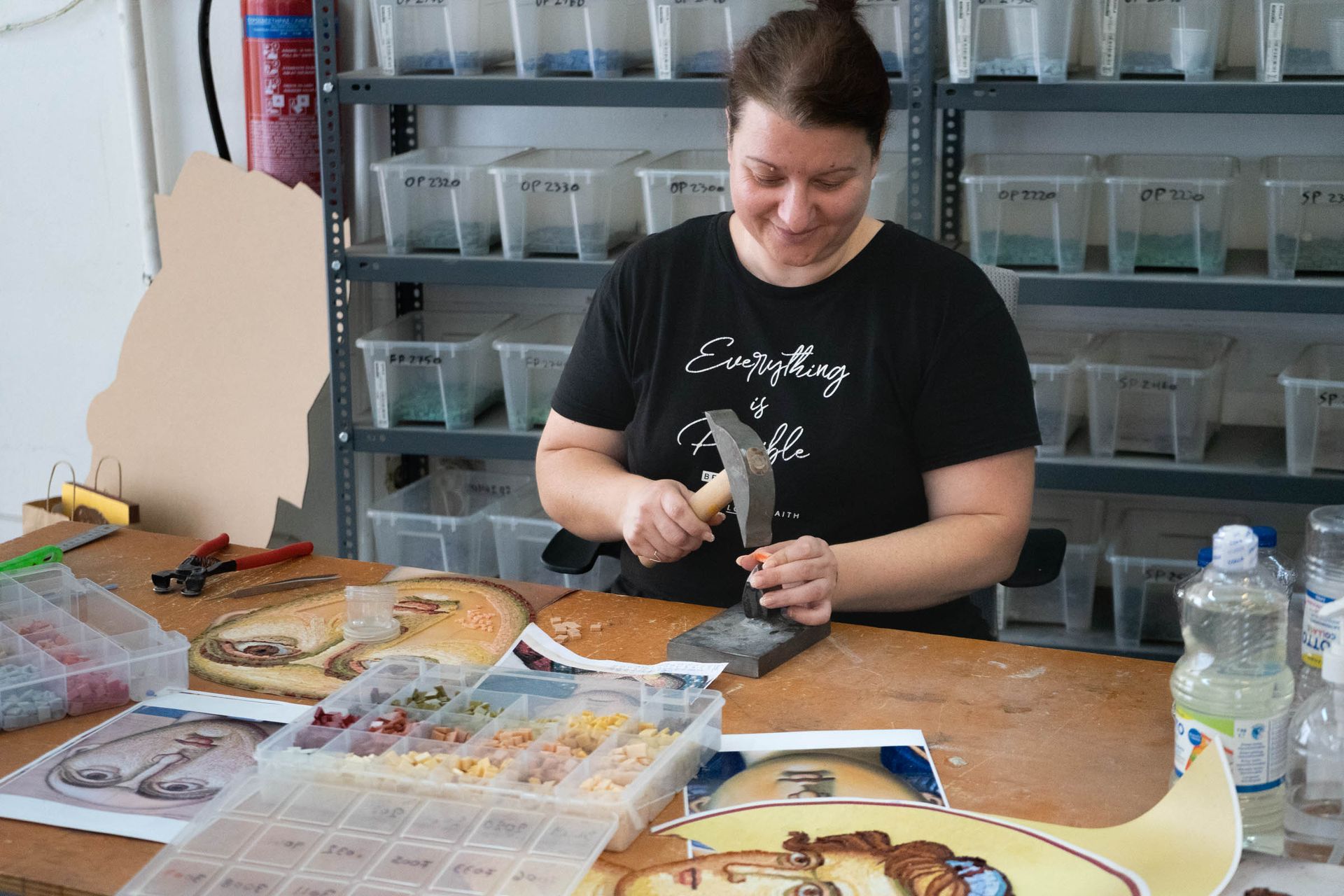 Artisan hand-cutting smalti tiles with hammer and die while creating Byzantine mosaic face of the Virgin Mary.
