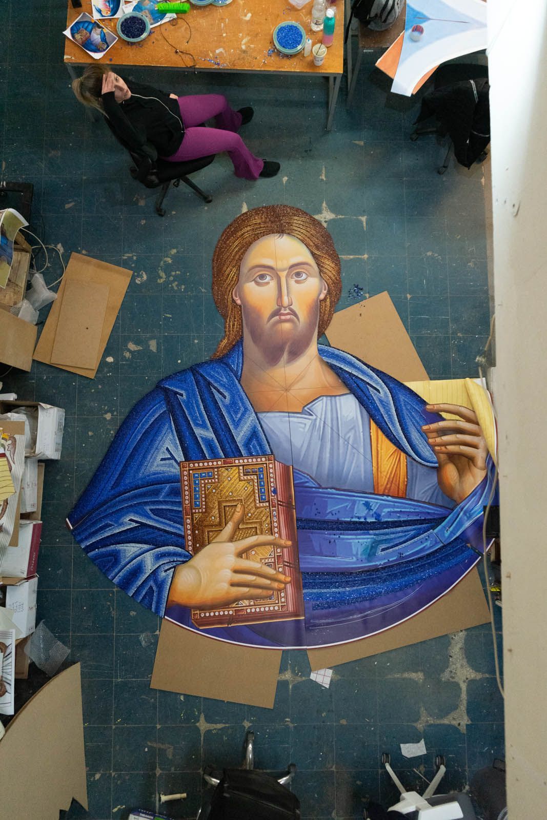 Large-scale Christ Pantocrator mosaic in progress at studio, artisan working beside oversized reverse-method Byzantine panel.