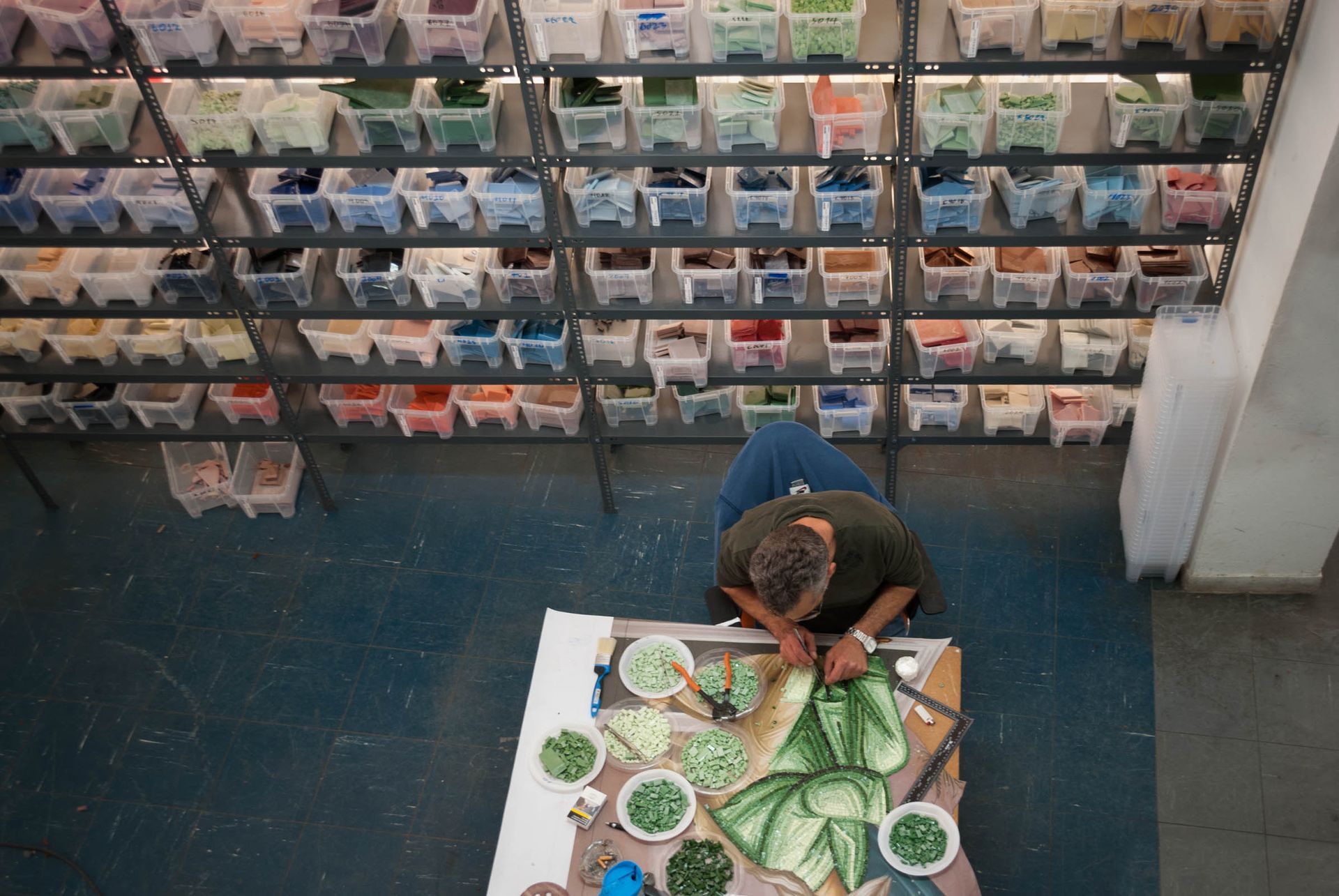 Byzantine Artworks artisan shaping green smalti tesserae in workshop with colorful smalti glass materials.