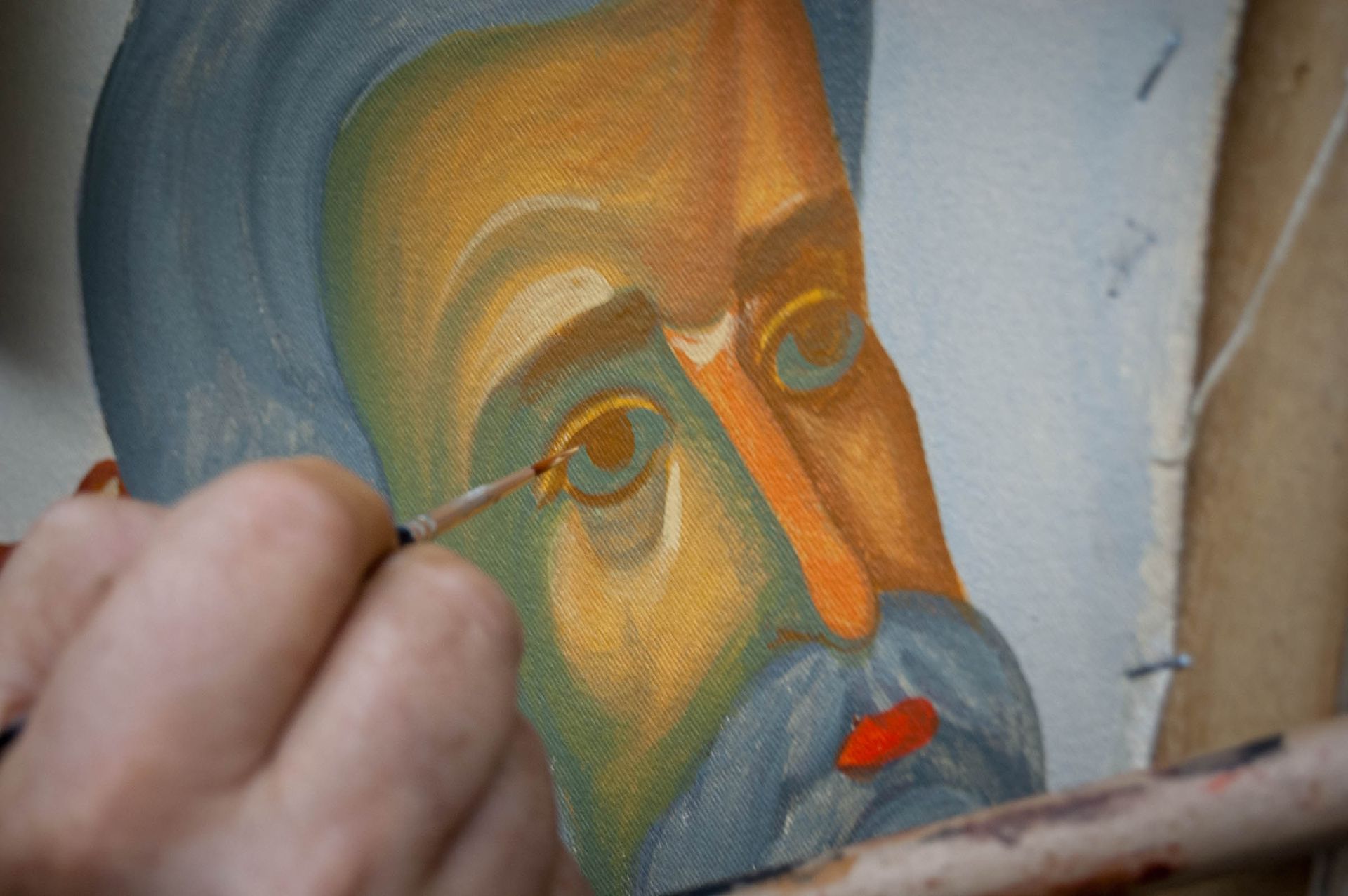 Close up of iconographer painting eye detail on Eastern Christian mural icon, hand and brush applying pigment on canvas.