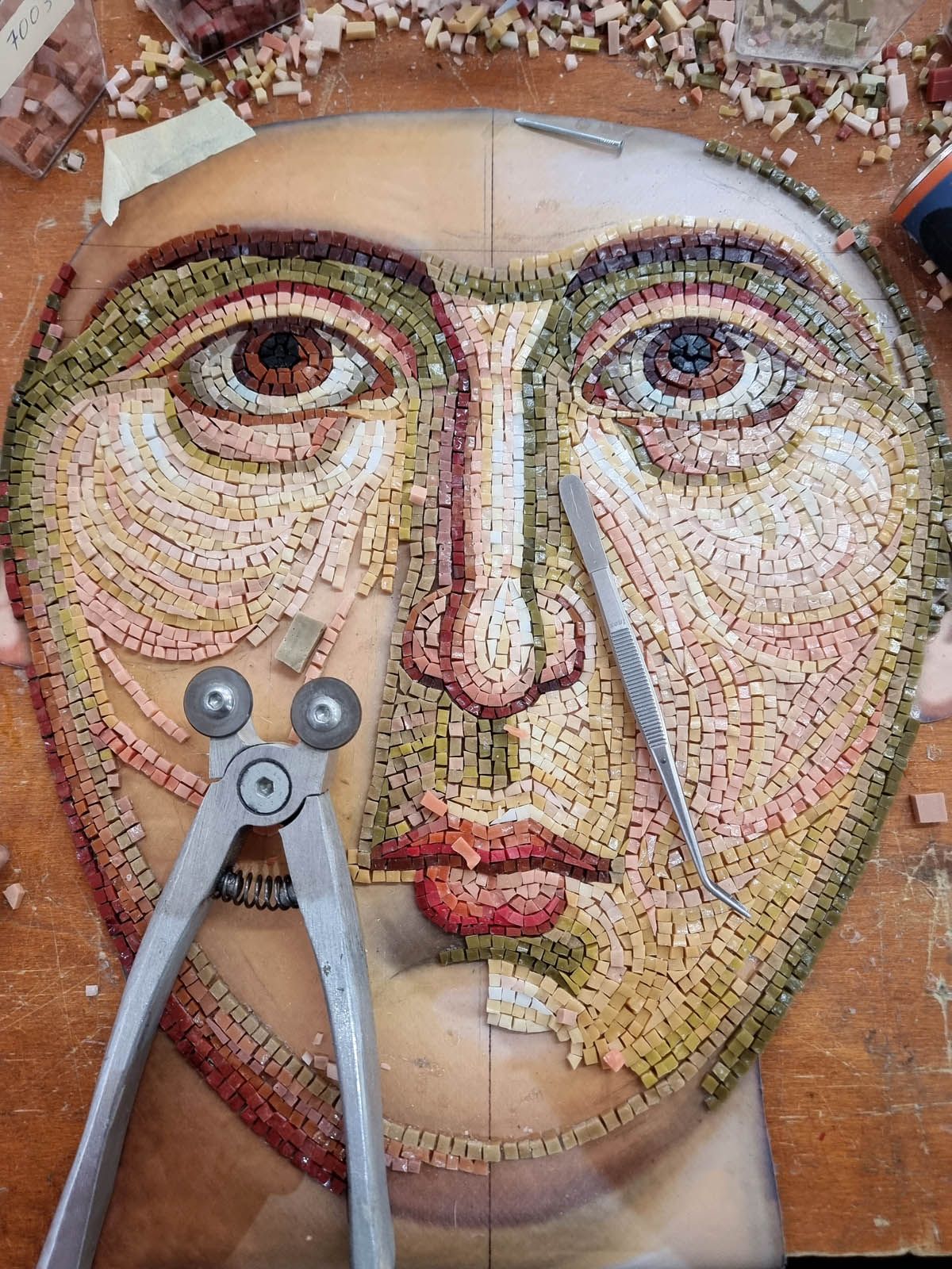 Hand-cut, hand-laid Italian smalti mosaic face with mosaic tile nippers during Byzantine mosaic crafting reverse process