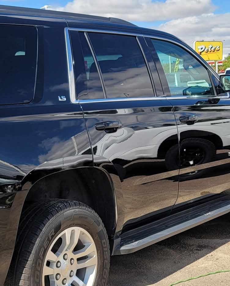 A person using a polishing machine on a dark gray car door, removing imperfections.