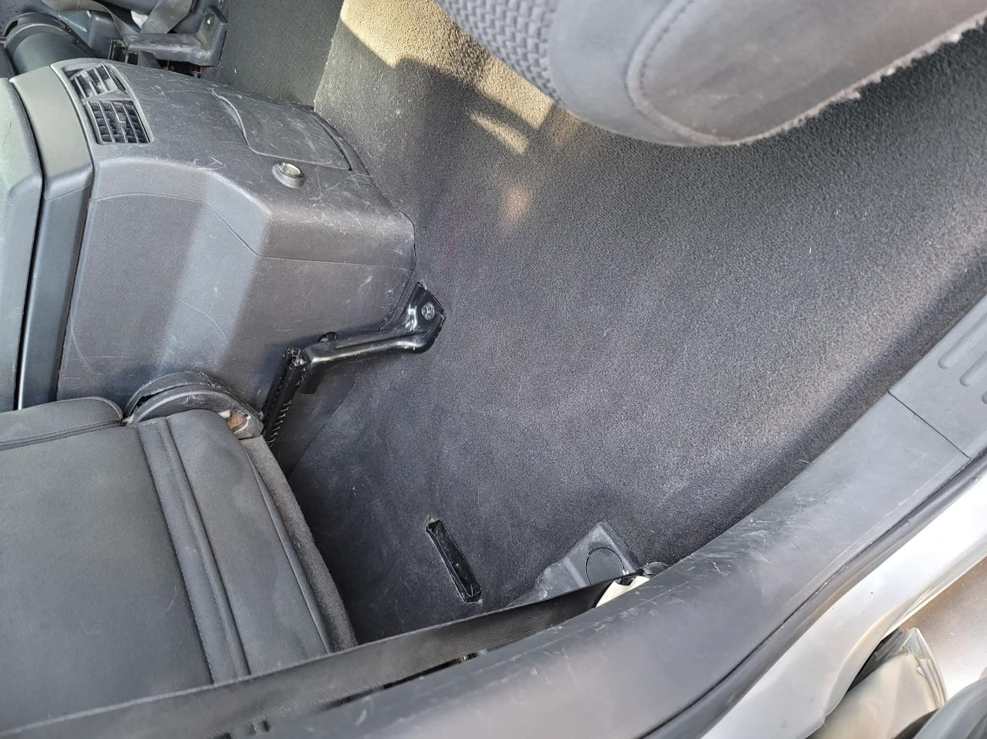 High-angle view of a vehicle floor covered in dark gray carpet, showing a car seat base and a central plastic console.