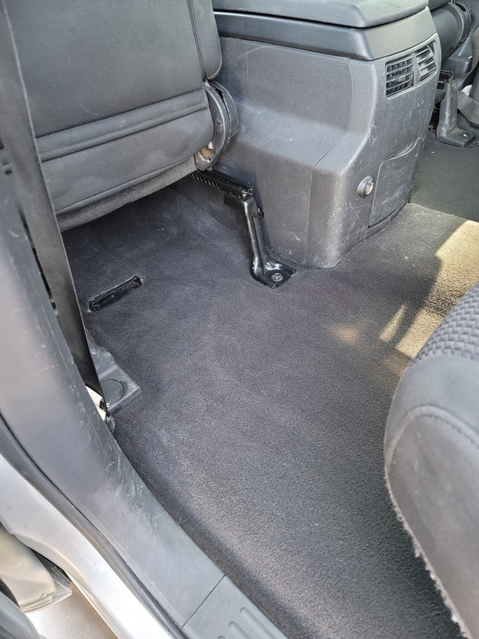 Floor area of a vehicle interior showing a black carpet, seat rail, and center console.
