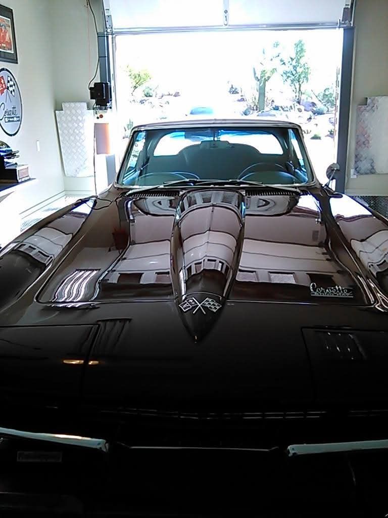The front view of a dark, glossy vintage Chevrolet Corvette parked inside a garage.