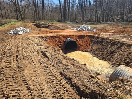 Construction site with a culvert pipe draining muddy water. Rocks and dirt piles surround the pipe.
