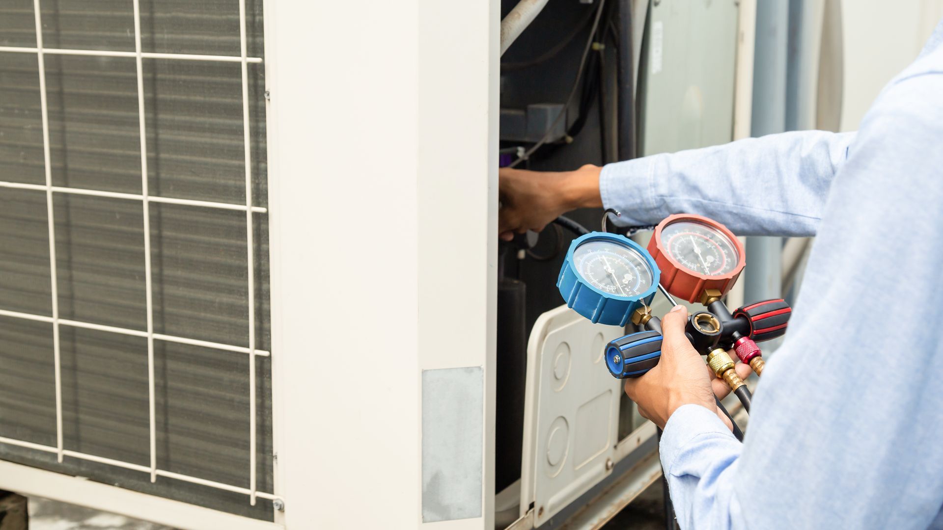 Technician checking HVAC system with gauges, inspecting refrigerant levels.