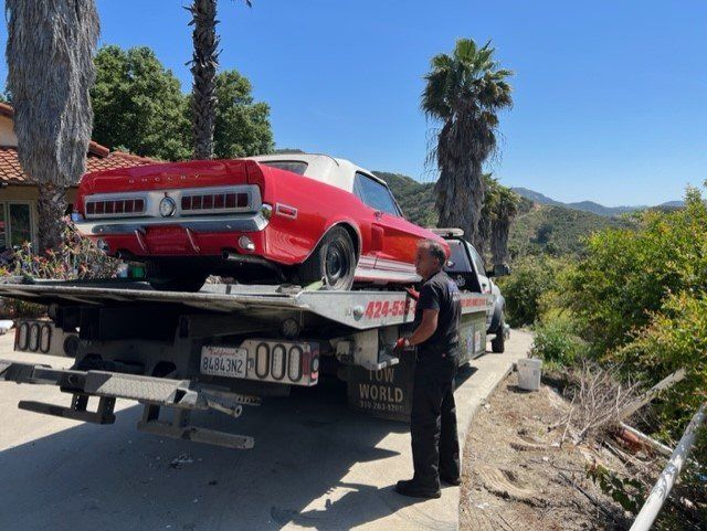 Red and white classic car on a tow truck, parked on a hill, with a man looking on.