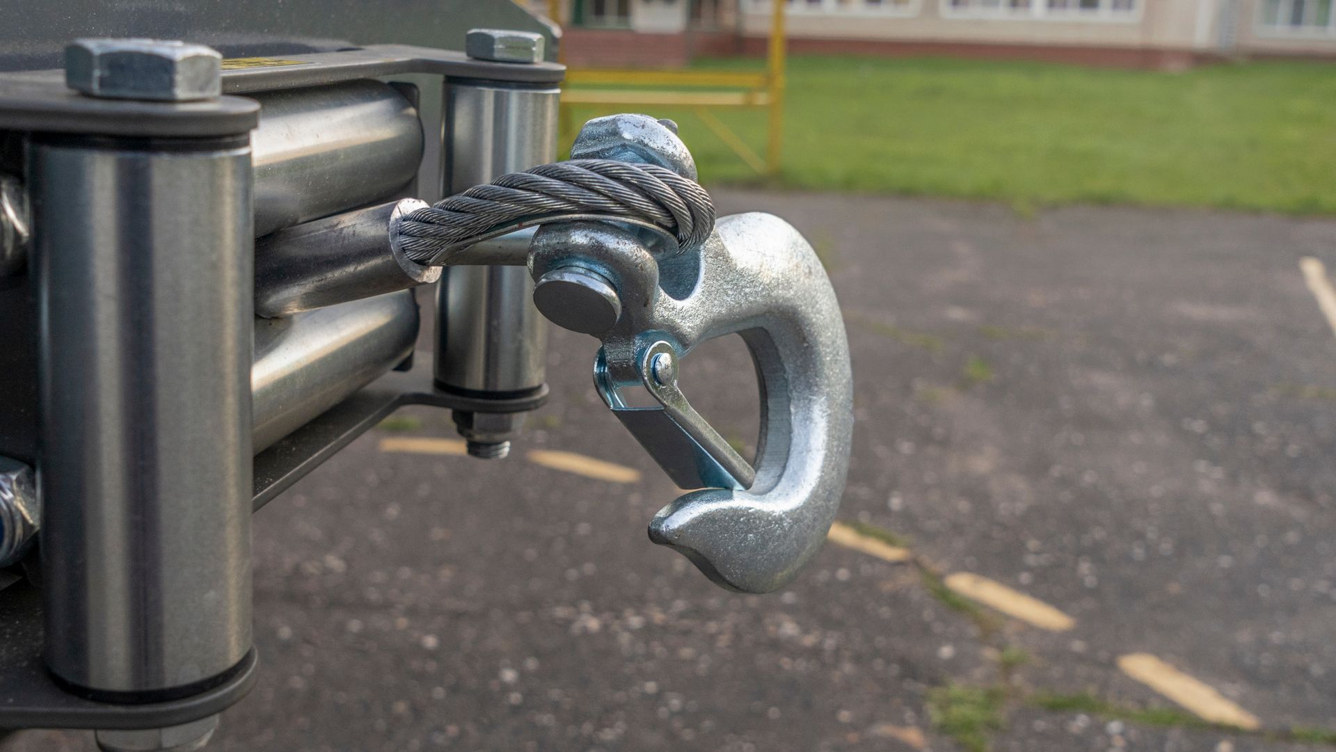 Close-up of a winch hook with cable attached to a metallic, silver winch mechanism in an outdoor setting.