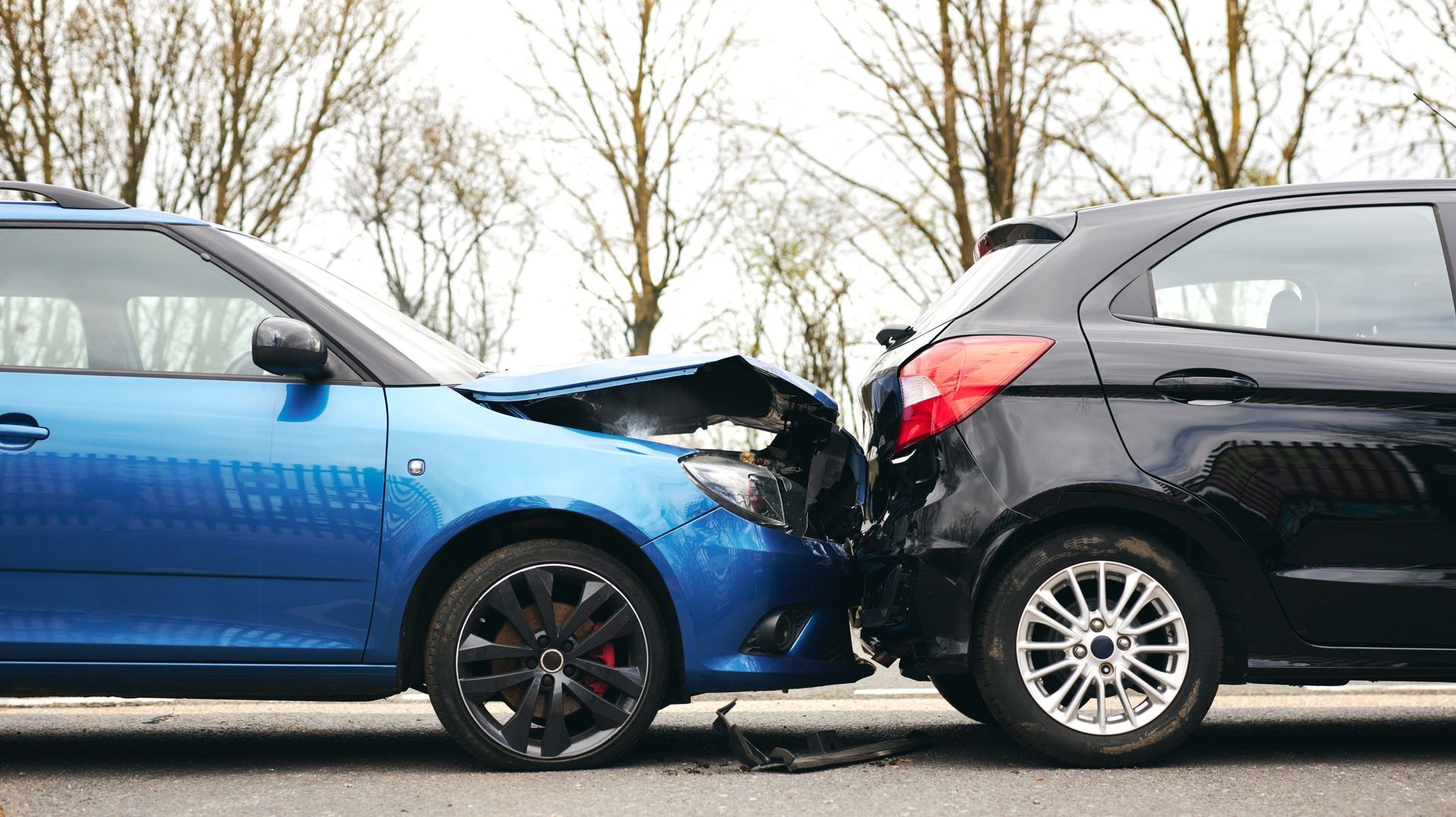 Two cars, blue and black, damaged in a collision on a road.