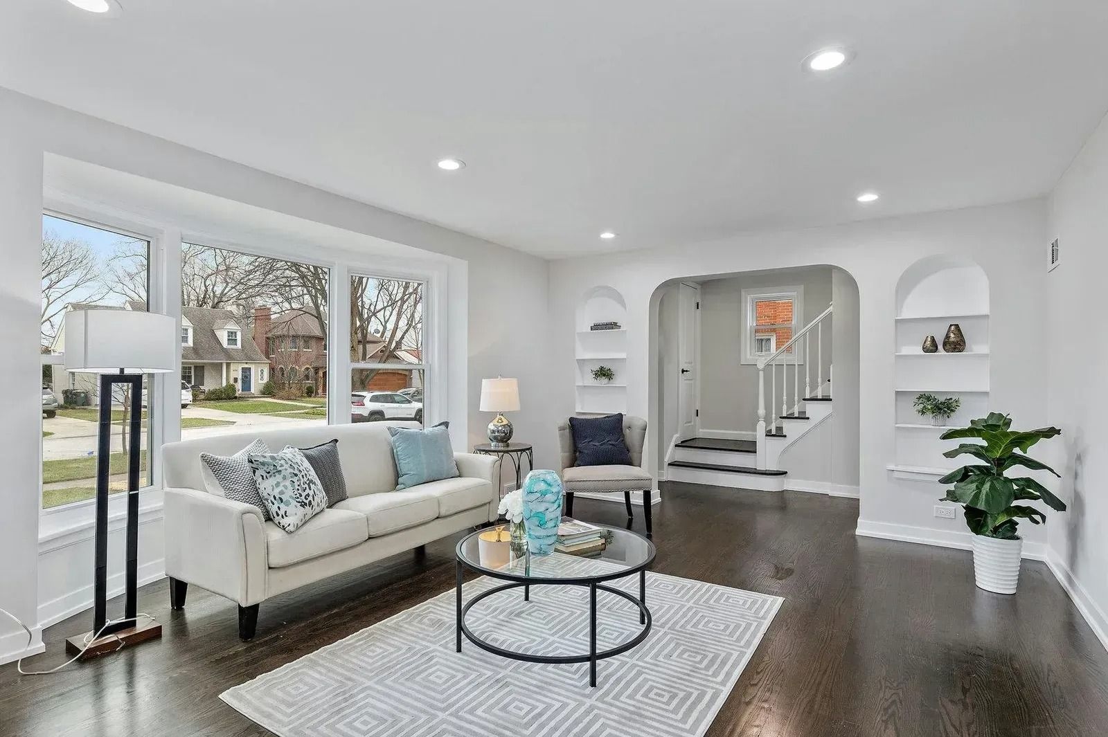 Living room with large window, white sofa, coffee table, and dark wood floors.