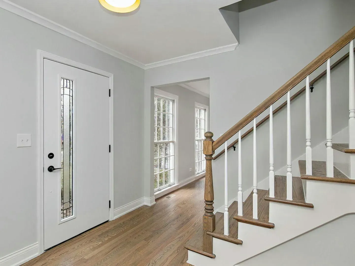 Entryway with a staircase, front door, and hallway with gray walls and wood flooring.