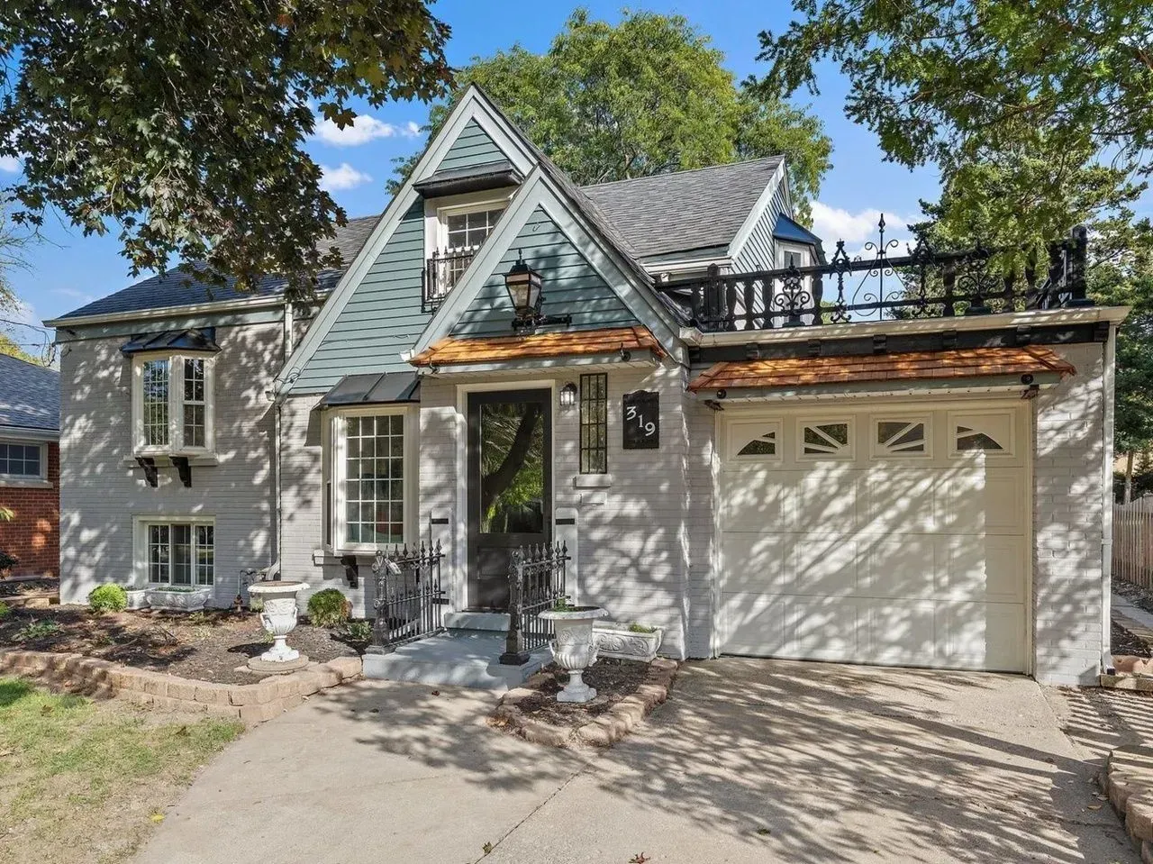 Gray house with blue-green accents, a black railing on the roof, and a white garage door.