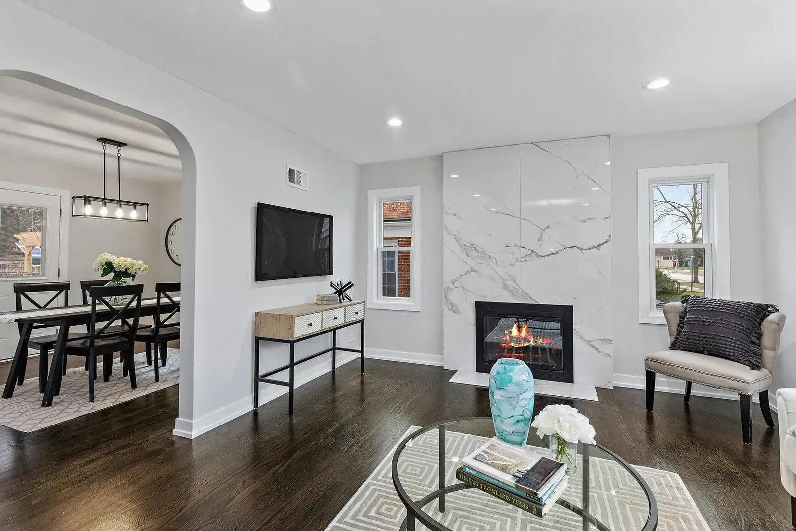 Living room with fireplace, TV, and dining area visible through an archway, hardwood floors.