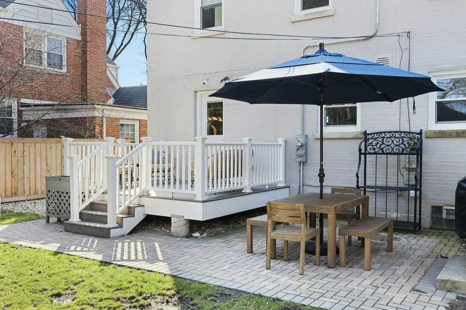 Backyard patio with a deck, table, umbrella, and decorative shelving against a white building.