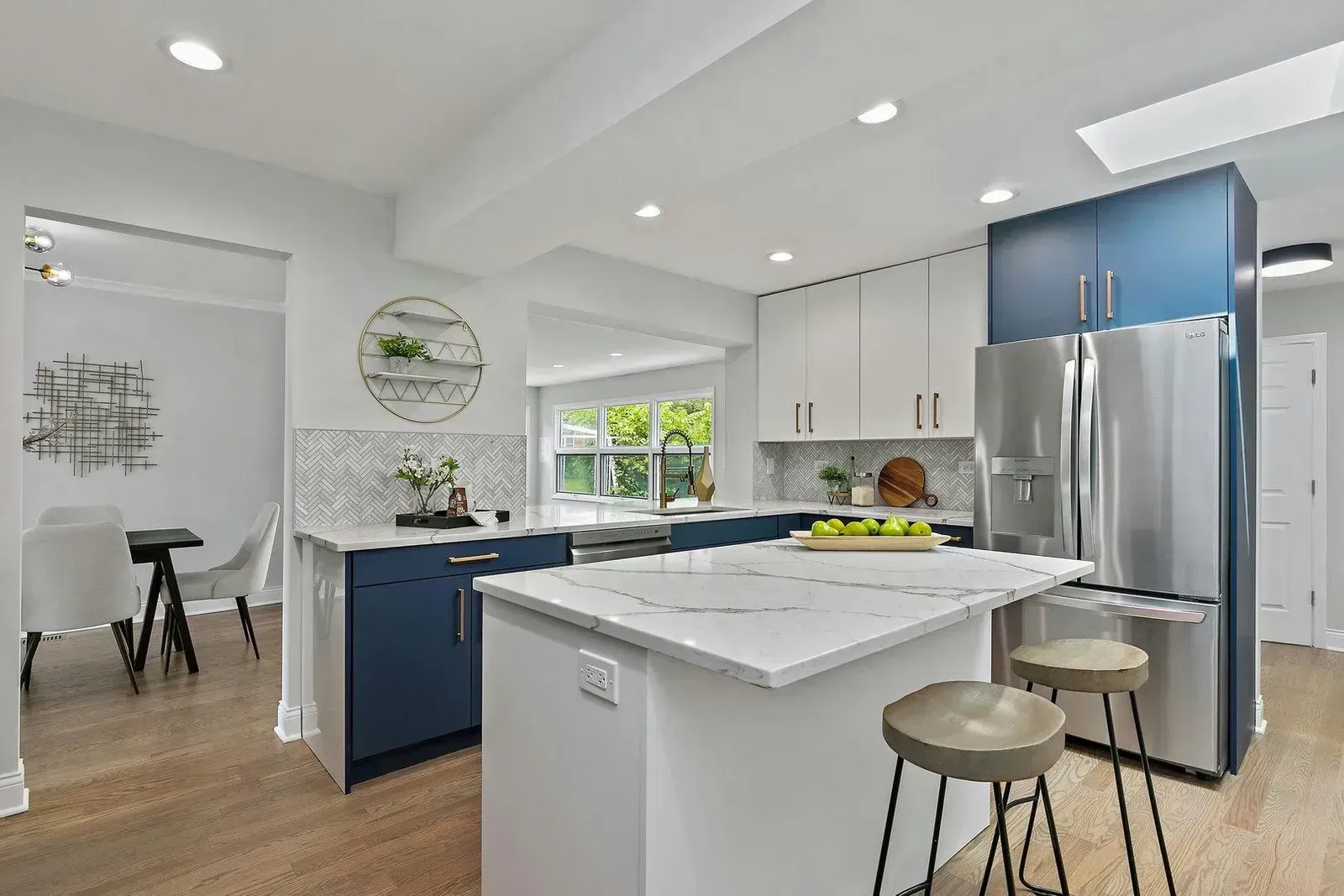 Modern kitchen with white and blue cabinets, island with stools, and stainless steel refrigerator.