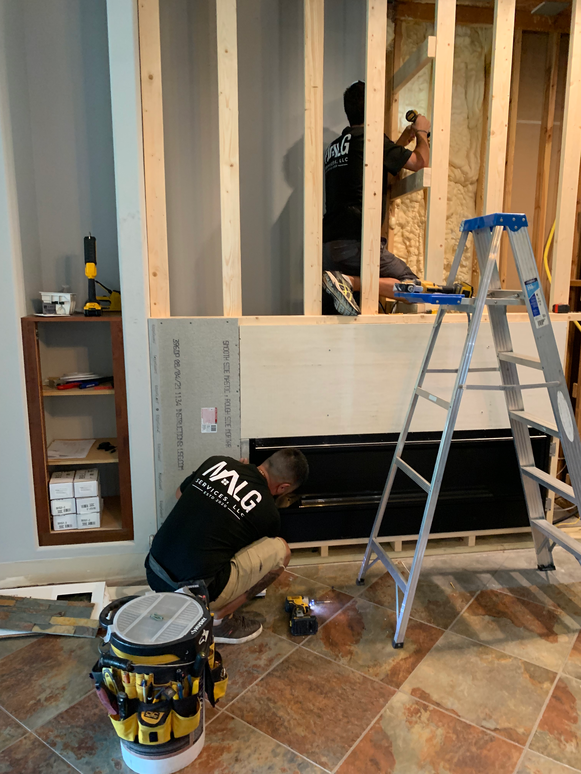 A man is working on a wall in a room next to a ladder.