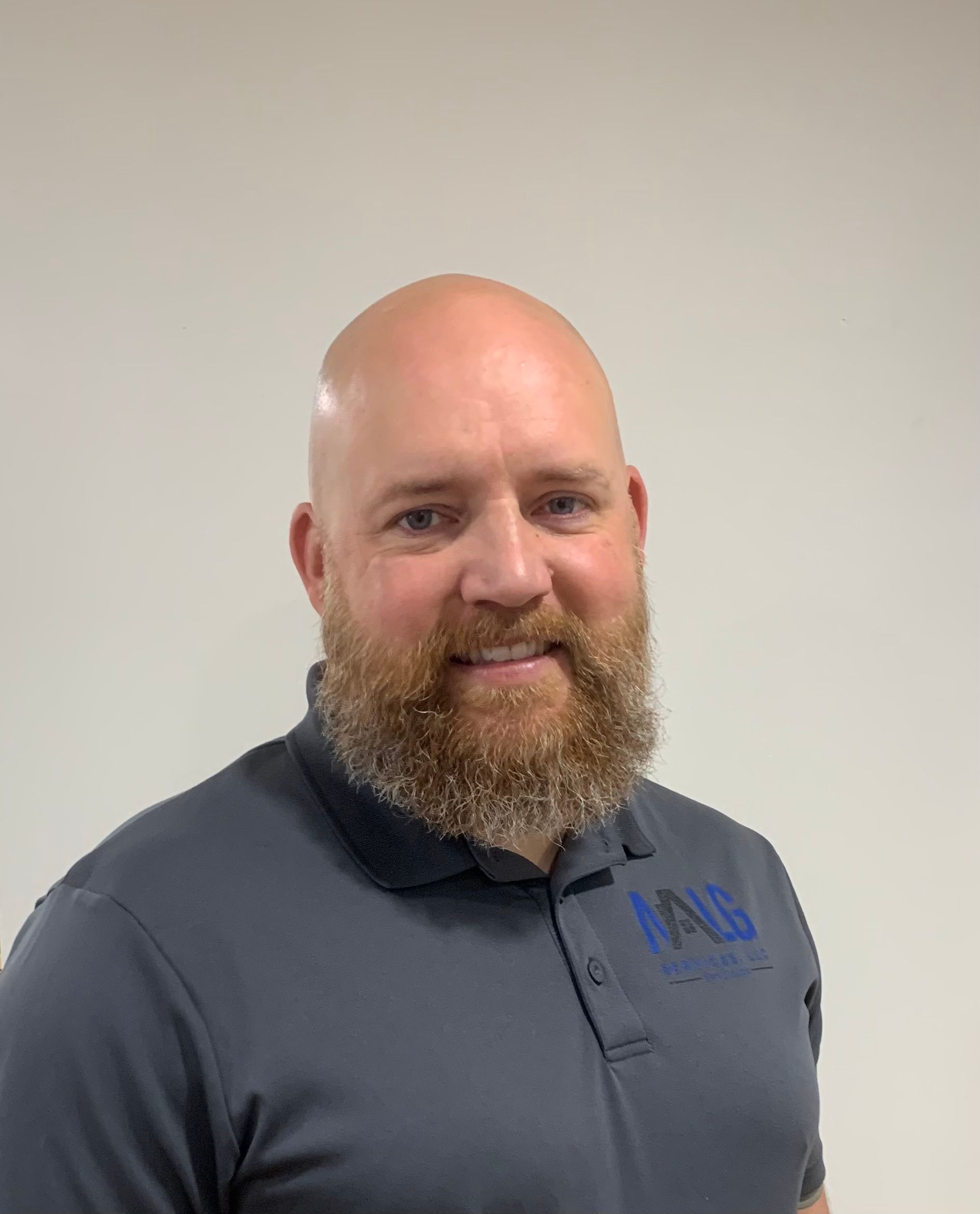 A bald man with a beard is wearing a gray polo shirt.