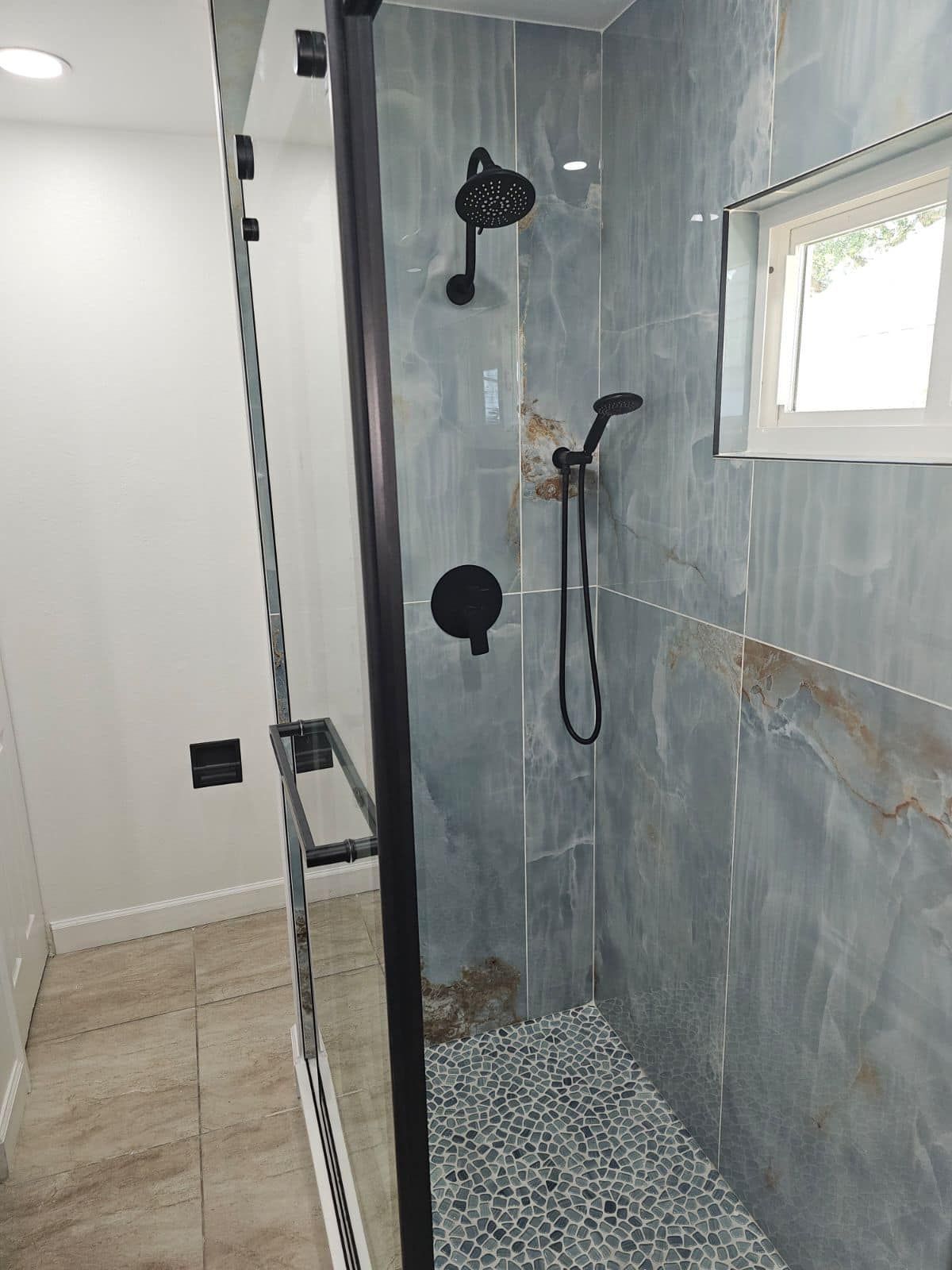 A bathroom with a walk in shower and a window.