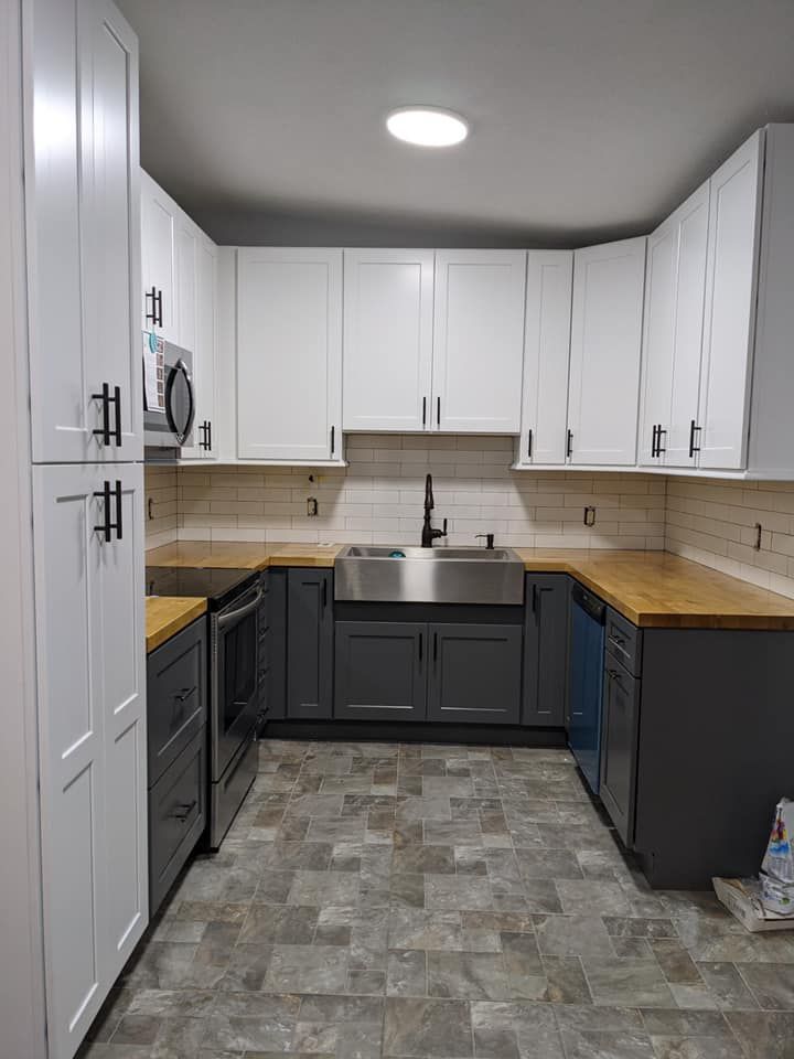 A kitchen with gray cabinets , white cabinets , wooden counter tops , a sink , and a microwave.