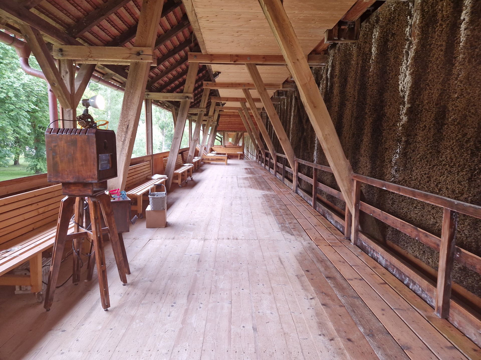 Ein überdachter Holzsteg mit Bänken. An einer Seite eine Salzwand. Ein hölzernes Instrument auf einem Dreibein.