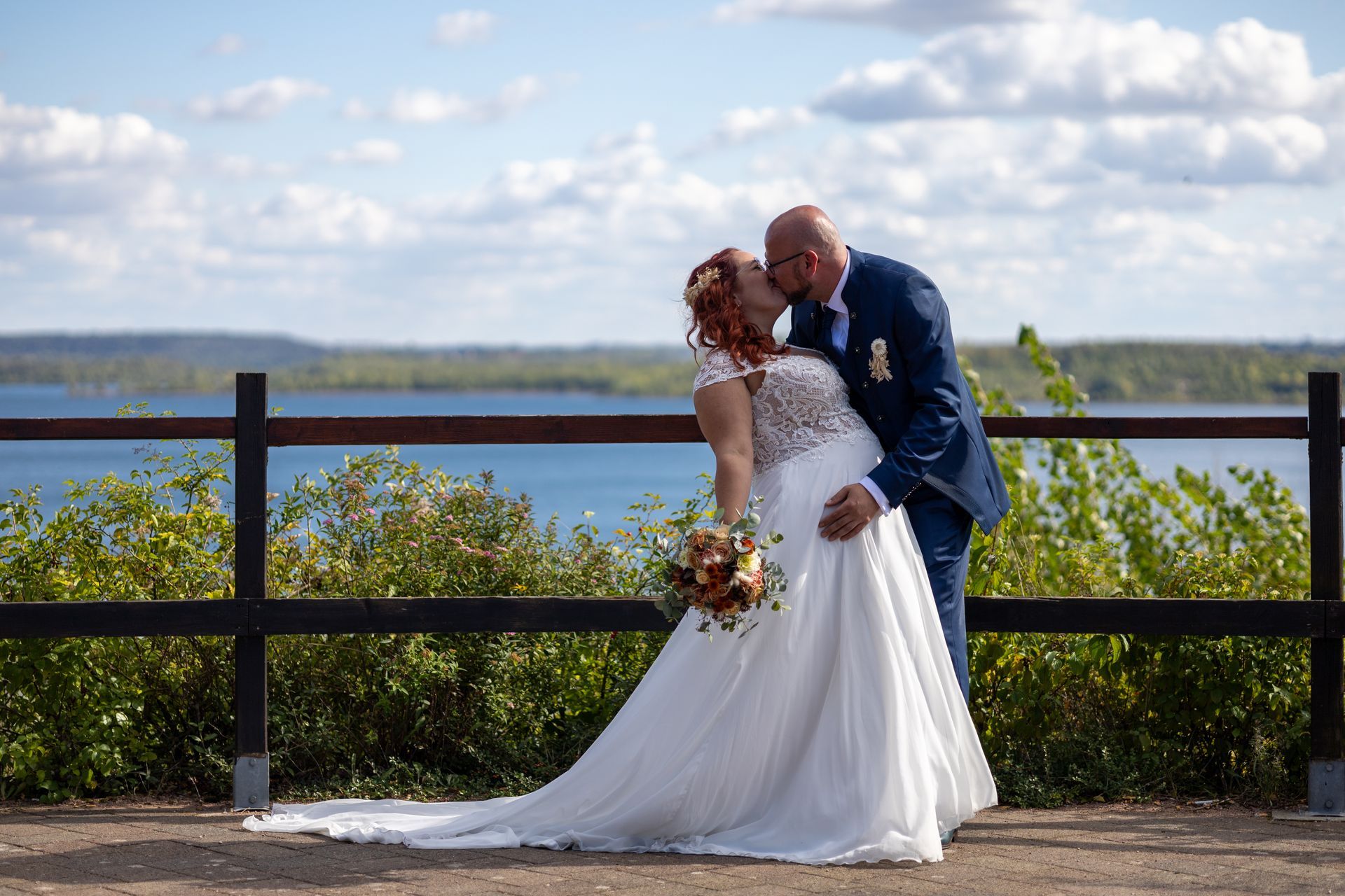 Eine Braut und ein Bräutigam küssen sich vor einem See.