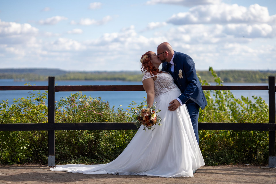Eine Braut und ein Bräutigam küssen sich vor einem See.