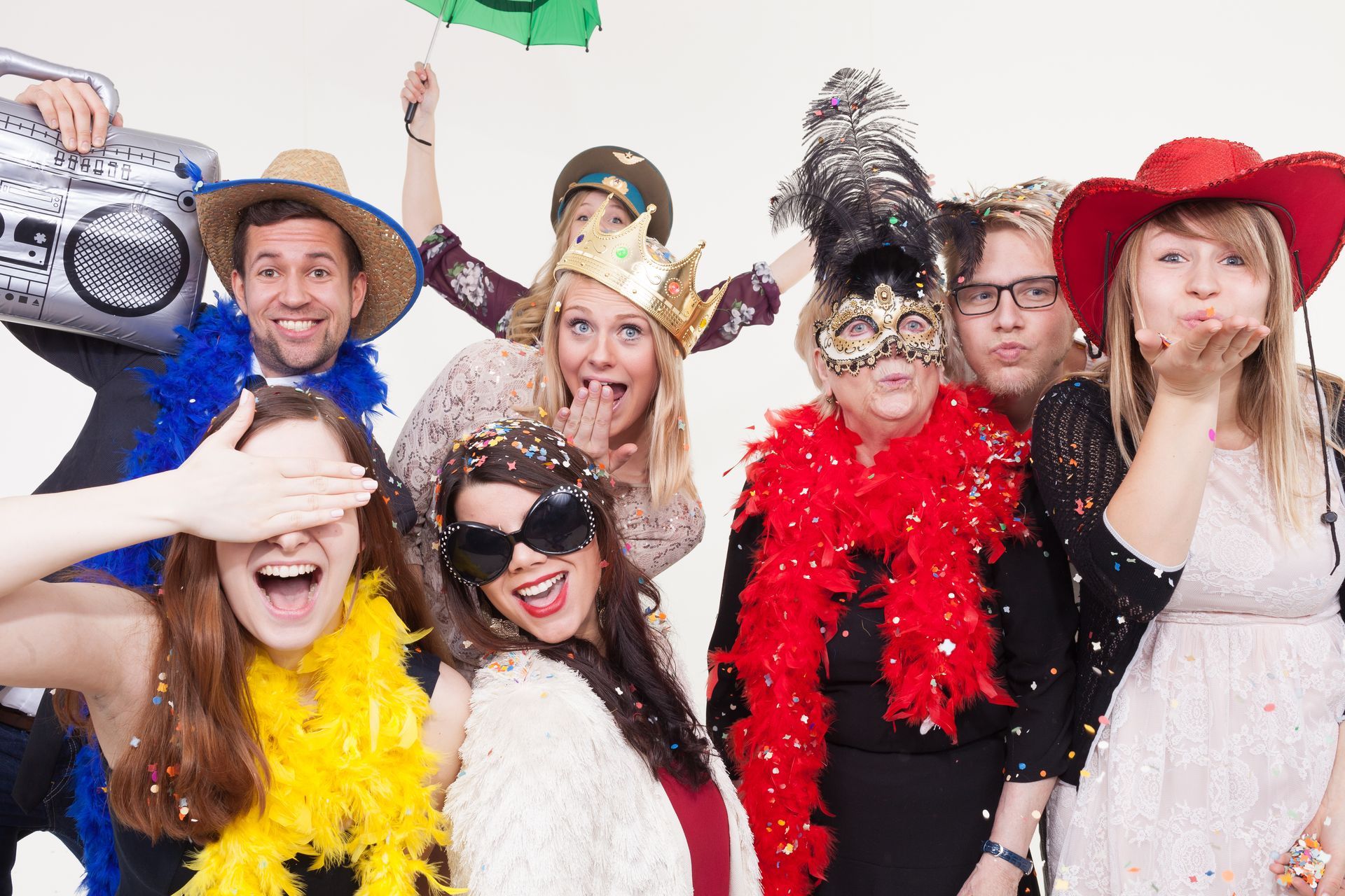 Eine Gruppe von Menschen in einer Fotokabine, die lustige Hüte und Brillen tragen und mit albernen Gesichtsausdrücken vor einem rosa Hintergrund posieren.