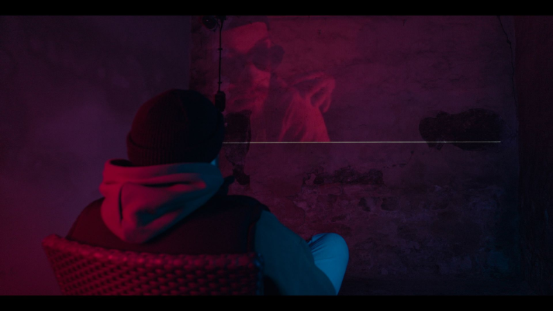 Ein Mann sitzt in einem dunklen Raum auf einem Stuhl vor einer Wand.