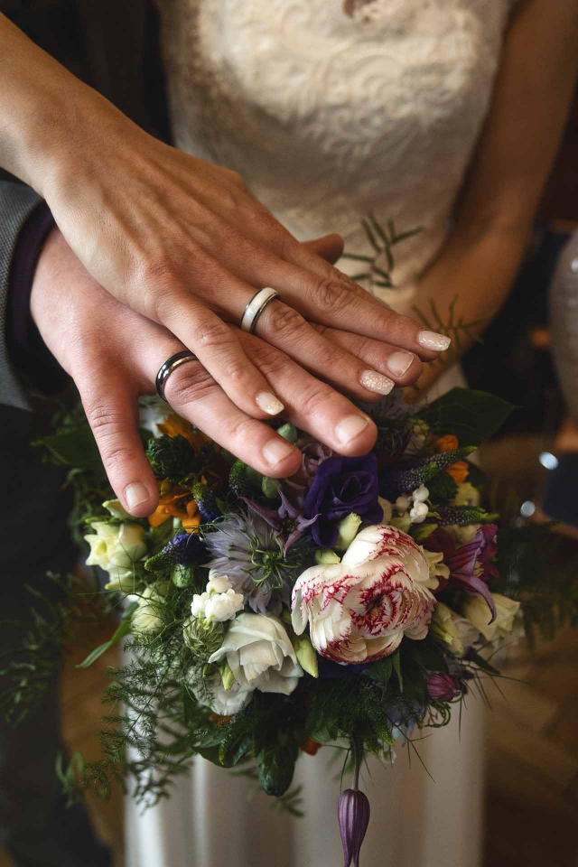 Eine Braut und ein Bräutigam halten einen Blumenstrauß und tragen ihre Eheringe.