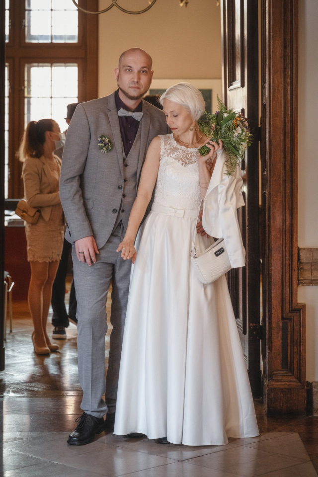 Eine Braut und ein Bräutigam stehen nebeneinander in einem Flur und halten Händchen.