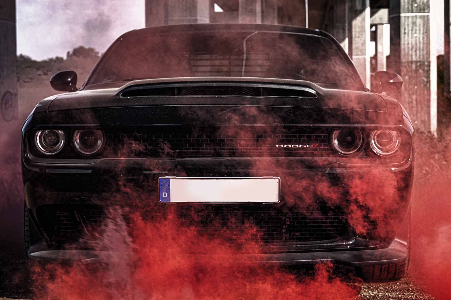 Ein schwarzes Auto, aus dessen Auspuff roter Rauch aufsteigt.