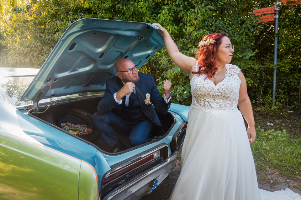 Eine Braut und ein Bräutigam posieren auf dem Rücksitz eines Autos für ein Foto.