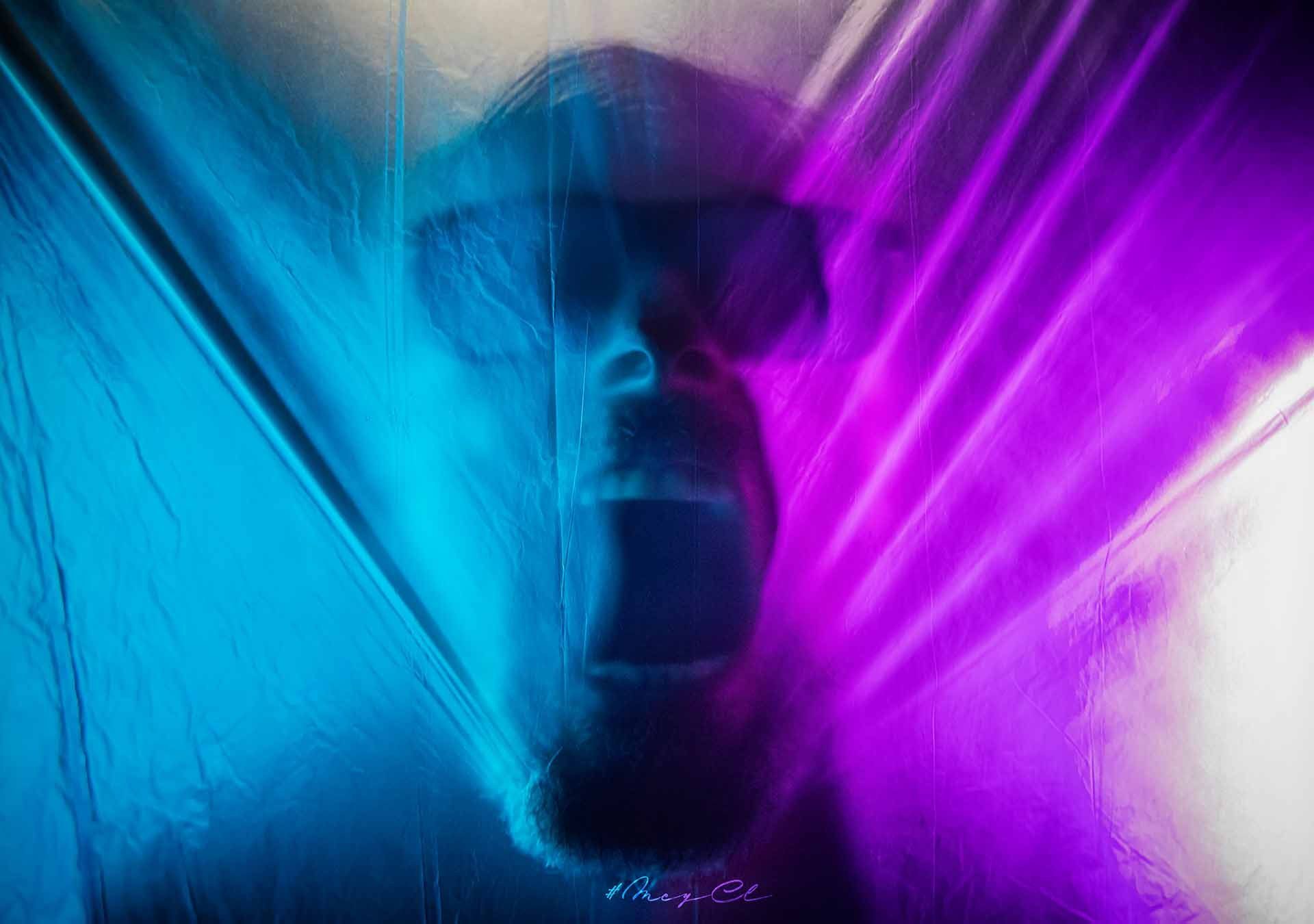 Ein Mann mit Bart und Sonnenbrille steht hinter einem blau-violetten Vorhang.