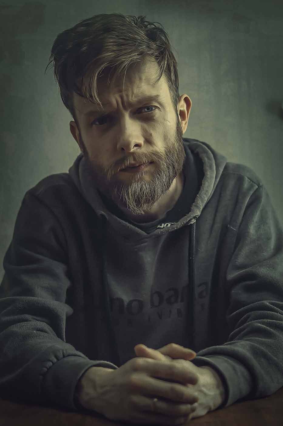 Ein Mann mit Bart sitzt mit gefalteten Händen an einem Tisch.