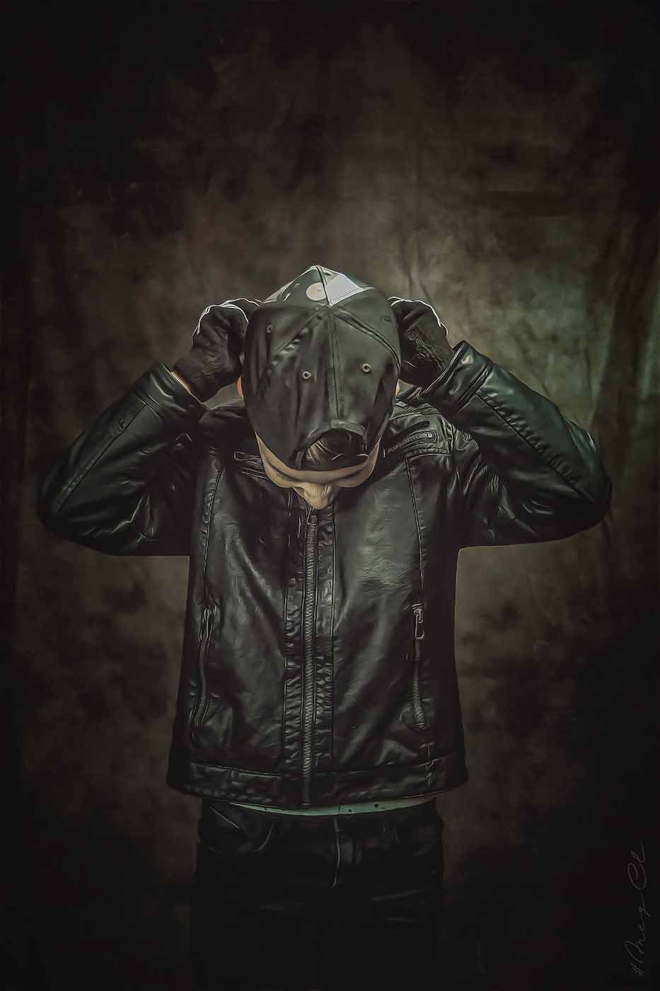 Ein Mann trägt eine schwarze Lederjacke und einen Hut und verdeckt sein Gesicht.