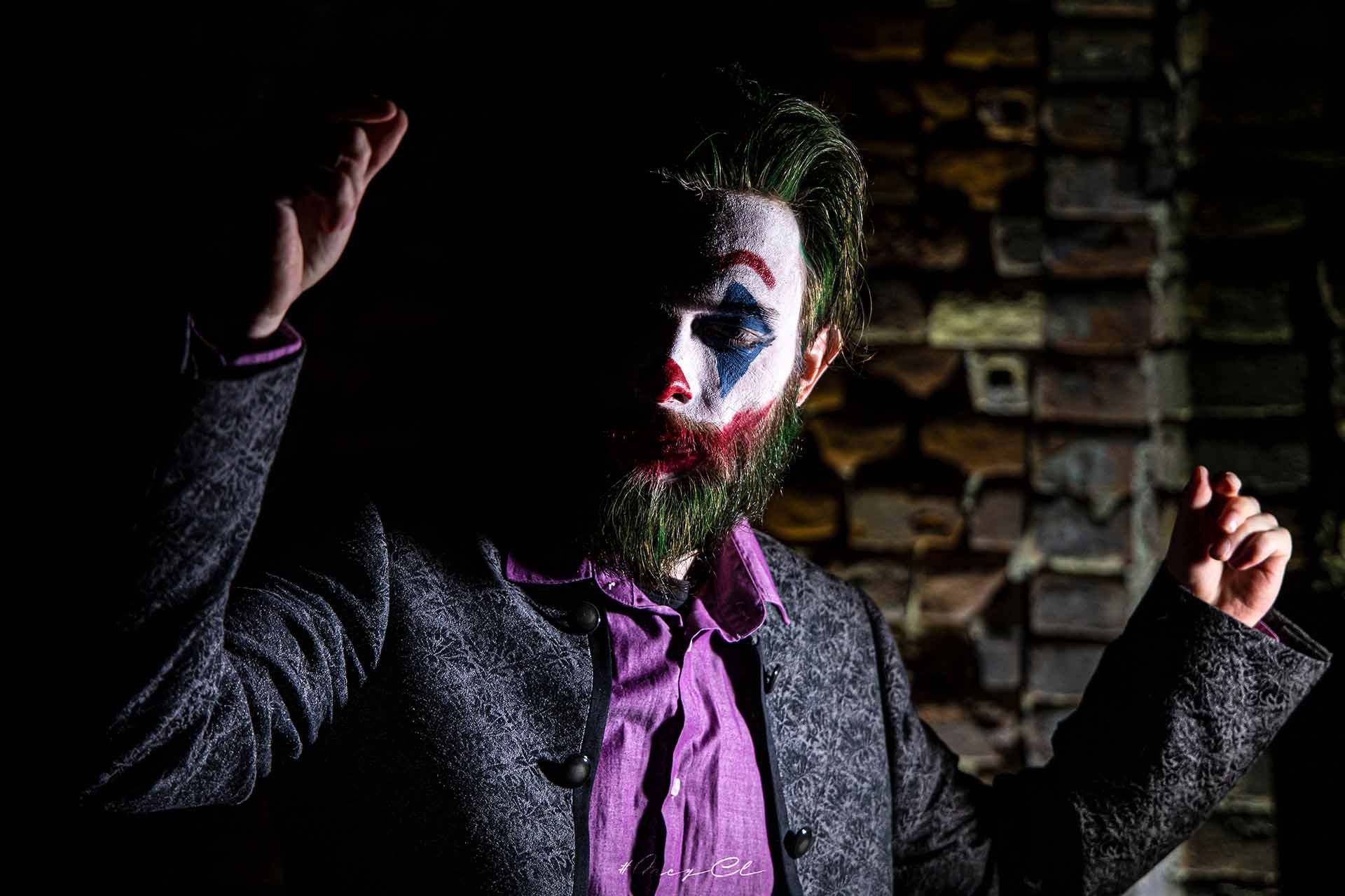 Ein als Joker verkleideter Mann mit Bart und Clown-Makeup steht in einem dunklen Raum.