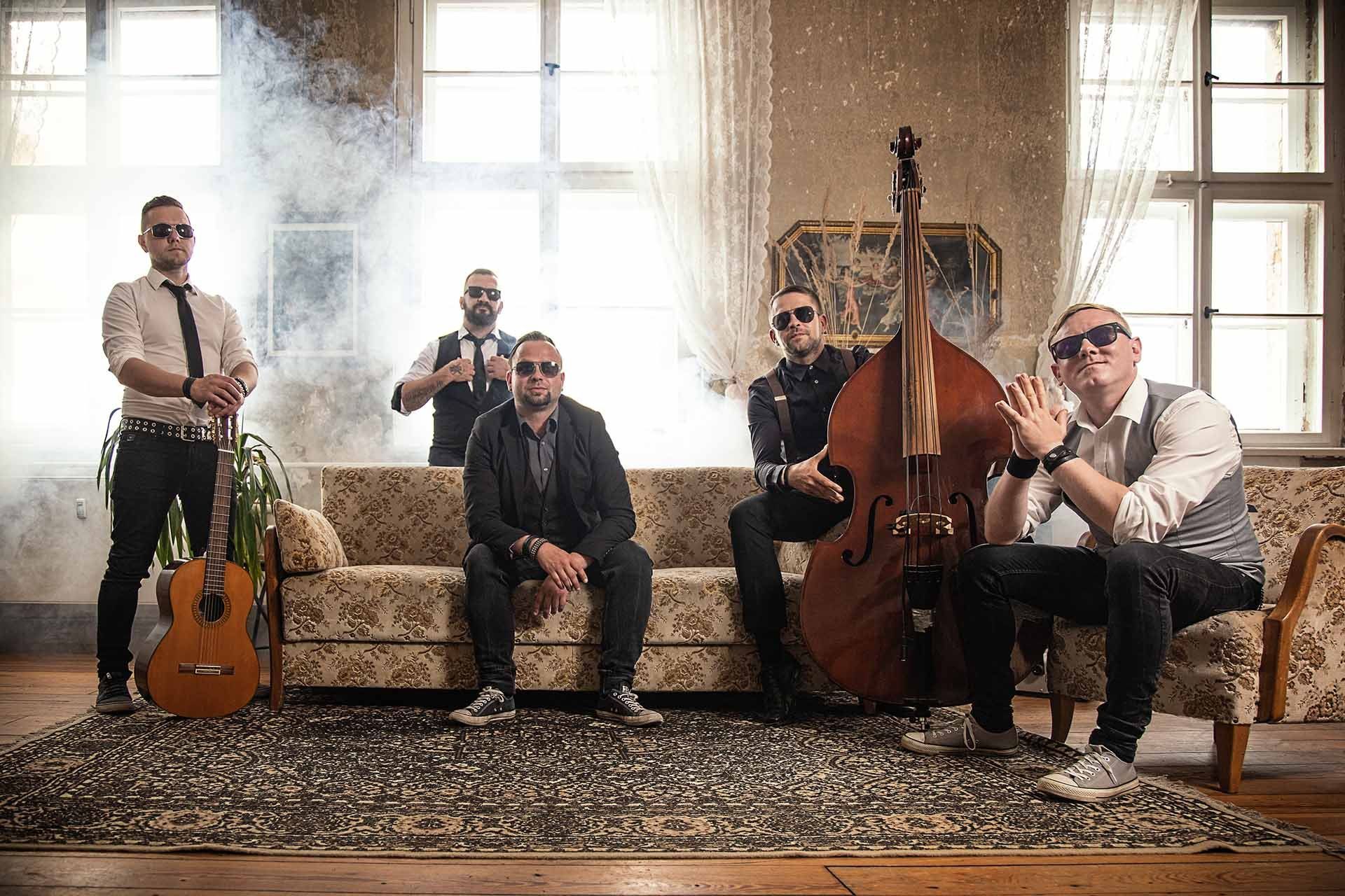 Eine Gruppe Männer sitzt auf einem Sofa und spielt Instrumente.