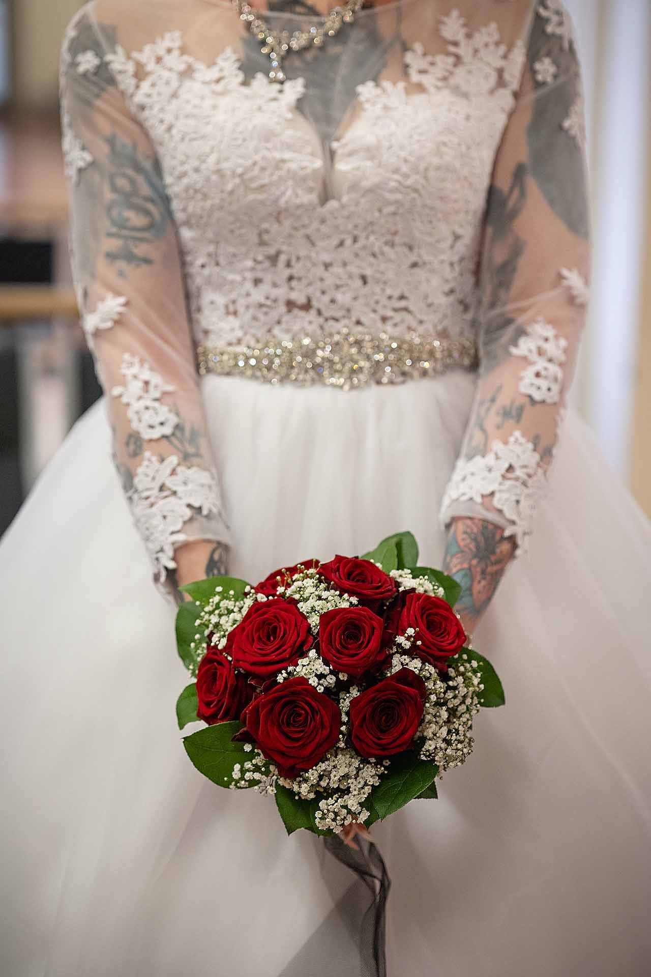 Eine Frau im Brautkleid hält einen Strauß roter Rosen.