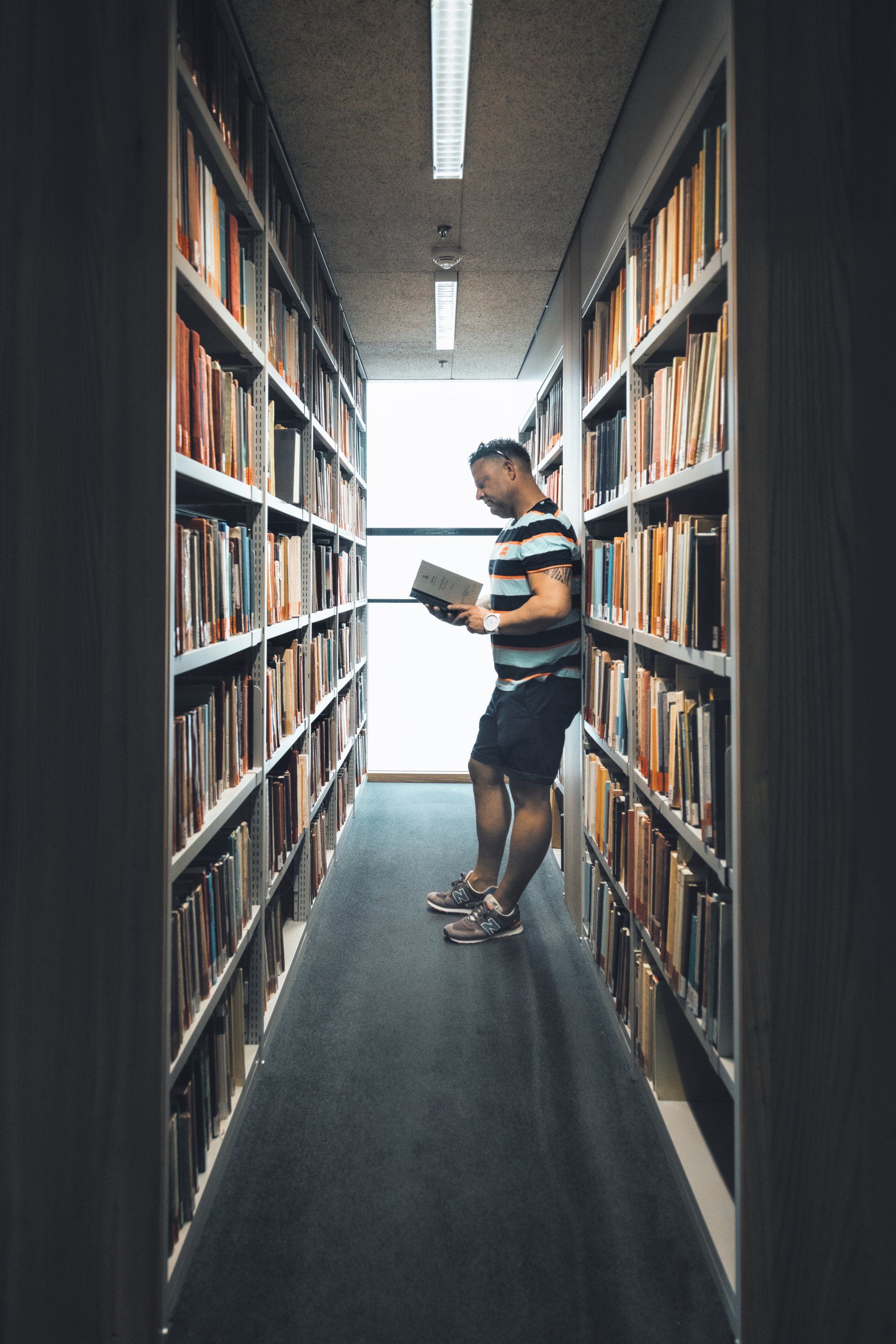 Ein Mann steht in einer Bibliothek und schaut sich ein Buch an.