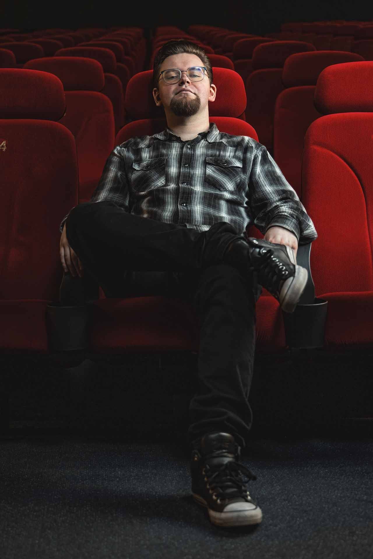 Ein Mann sitzt in einer Reihe roter Sitze in einem Theater.