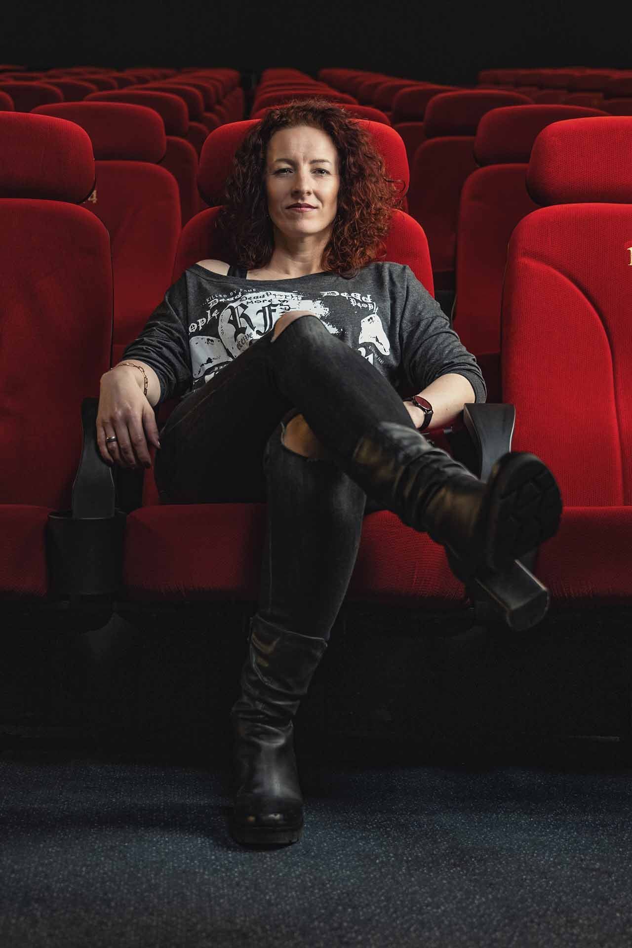 Eine Frau sitzt in einem Kino auf einem roten Stuhl.