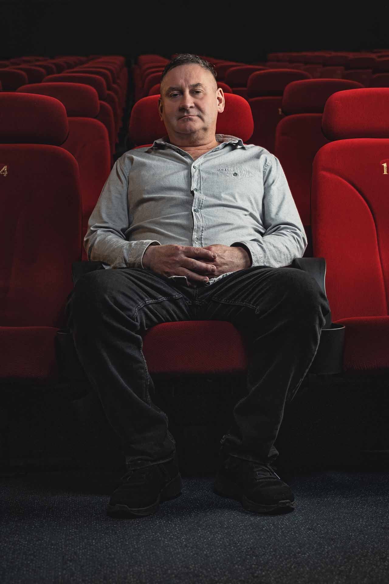 Ein Mann sitzt in einer Reihe roter Sitze in einem Kino.