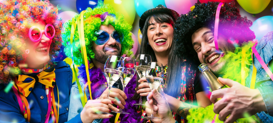 Feiernde Gäste in bunten Kostümen mit lustigen Requisiten vor der Fotobox auf einer Karnevalsparty